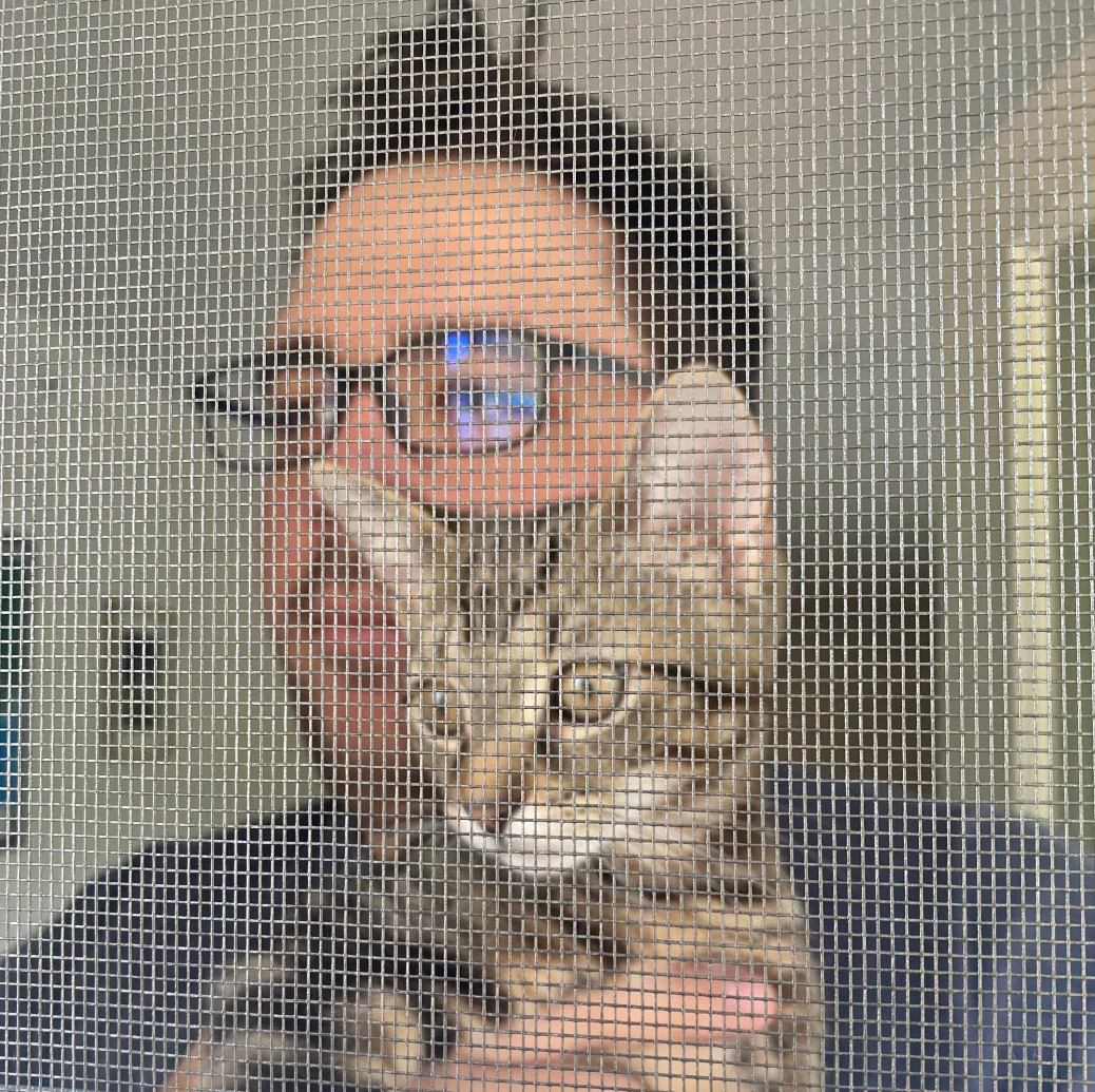Picture of Greg Siekman on the other side of a screen, looking into the distance holding his brown tabby cat Chauncey who is doing the same.